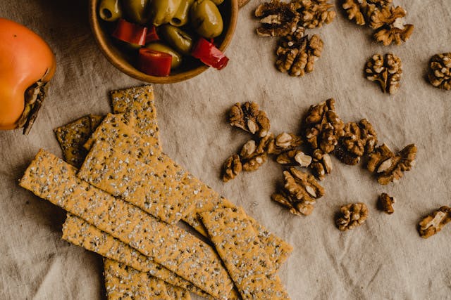 flaxseed & chia seed crackers on cloth with scattered walnuts, a capsicum and bowl of green olives
