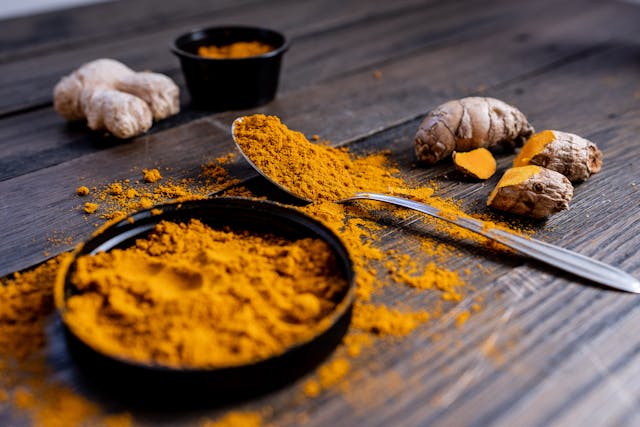 turmeric root next to turmeric ground on spoon and in bowl